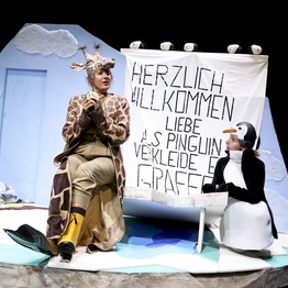 Szene aus "Viele Grüße, deine Giraffe" mit zwei  Personen verkleidet als Pinguin und Giraffe.
