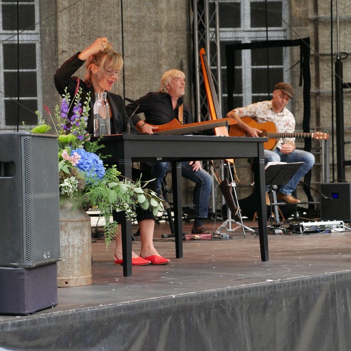 Schauspielerin Anna Schudt liest auf einer Bühne. Im Hintergrund sitzen zwei Musiker. (öffnet vergrößerte Bildansicht)