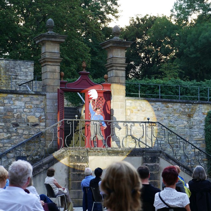 Der Schauspieler Nico Holonics steht als Oscar Matzerath auf einem Treppenabsatz des Ehrenhofs neben der Bühne und hält eine Trommel hoch. (öffnet vergrößerte Bildansicht)