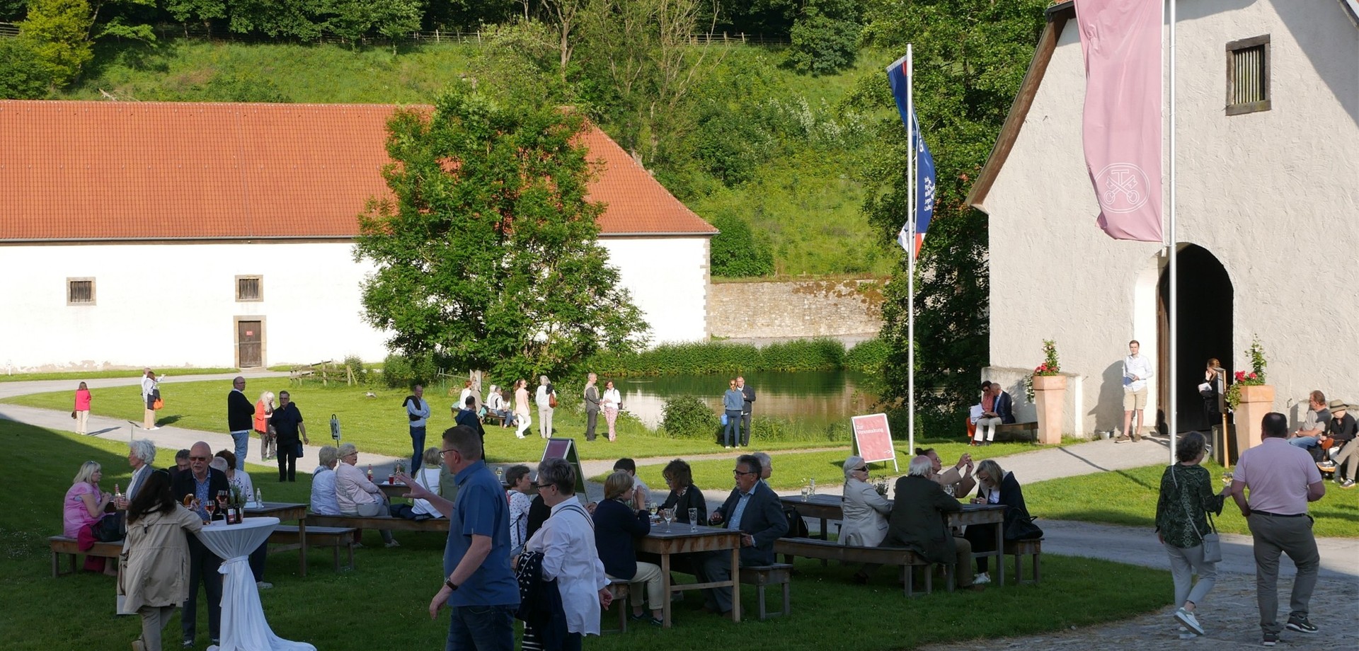 Blick auf den Eingang des Neuen Schafstalls mit Sitzmöglichkeiten und Stehtischen auf dem Rasen