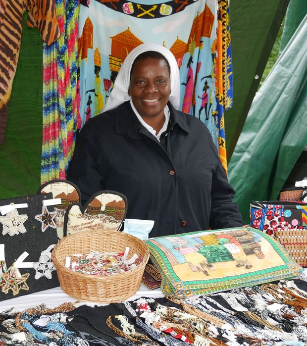 Eine farbige Ordensfrau steht an einem Stand mit vielen bunten Afrika-Waren.