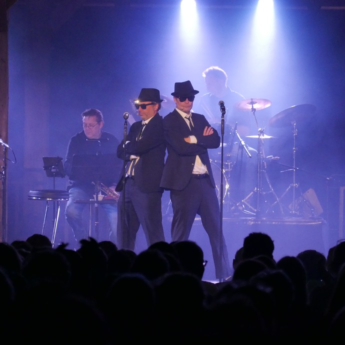 Bühnensituation auf der Show "Blues Brothers". Harald Schwaiger und Michael Kamp stehen Rücken an Rücken und schauen zum Publikum. (vergrößerte Bildansicht wird geöffnet)